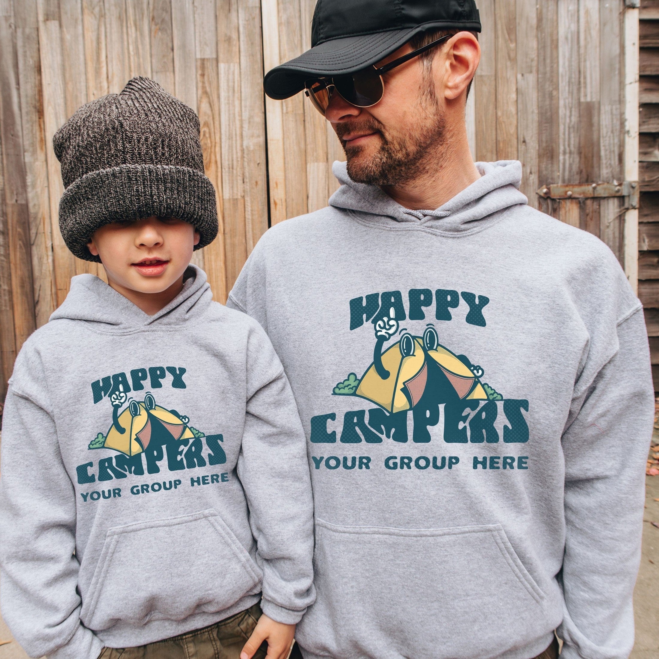 man and boy wearing custom matching family adventure vacation shirt with retro mascot style Happy Camper cartoon design. Perfect for group camping trips. Shown on gray hoodies