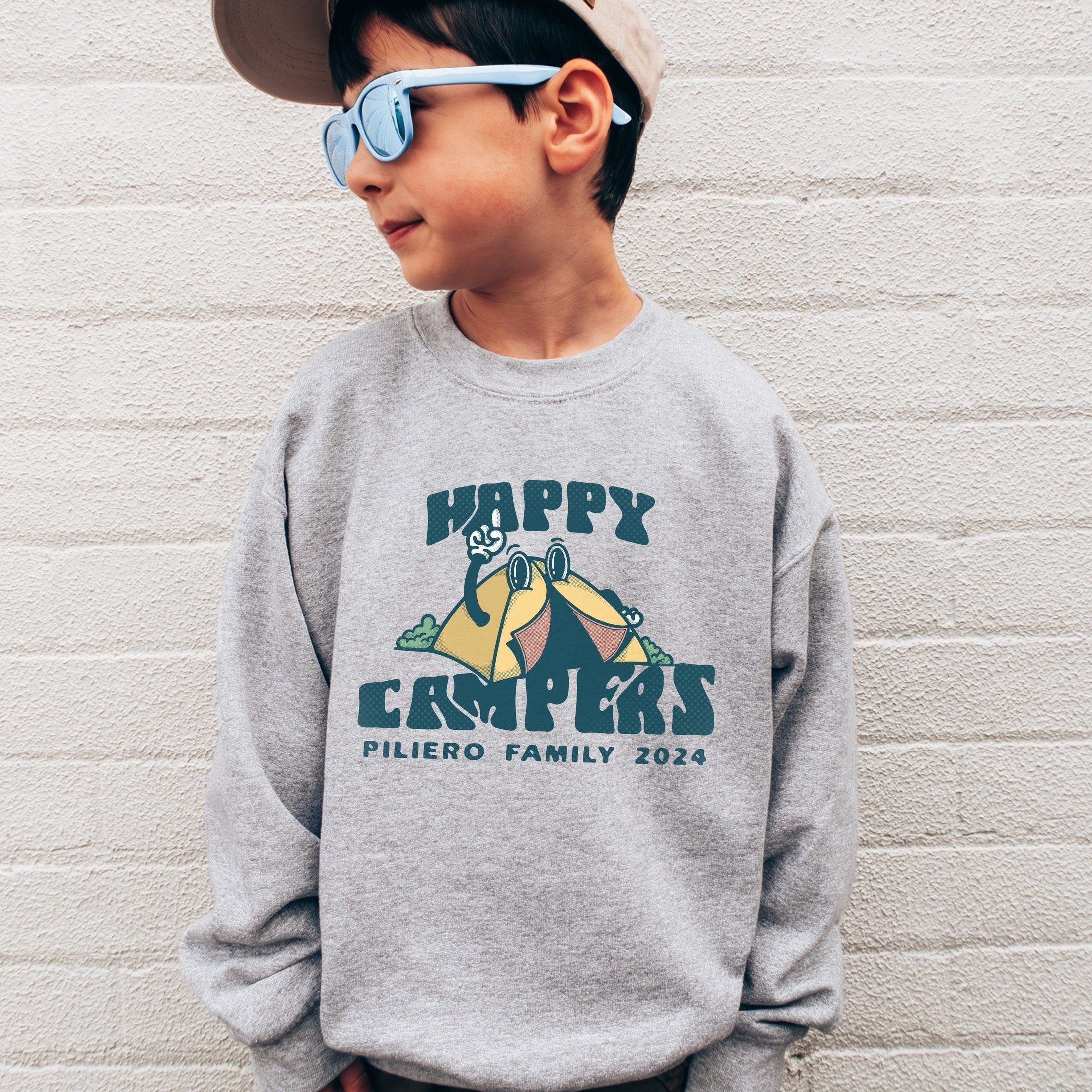 boy wearing custom matching family adventure vacation shirt with retro mascot style Happy Camper cartoon design. Perfect for group camping trips. Shown on gray crewneck sweatshirt