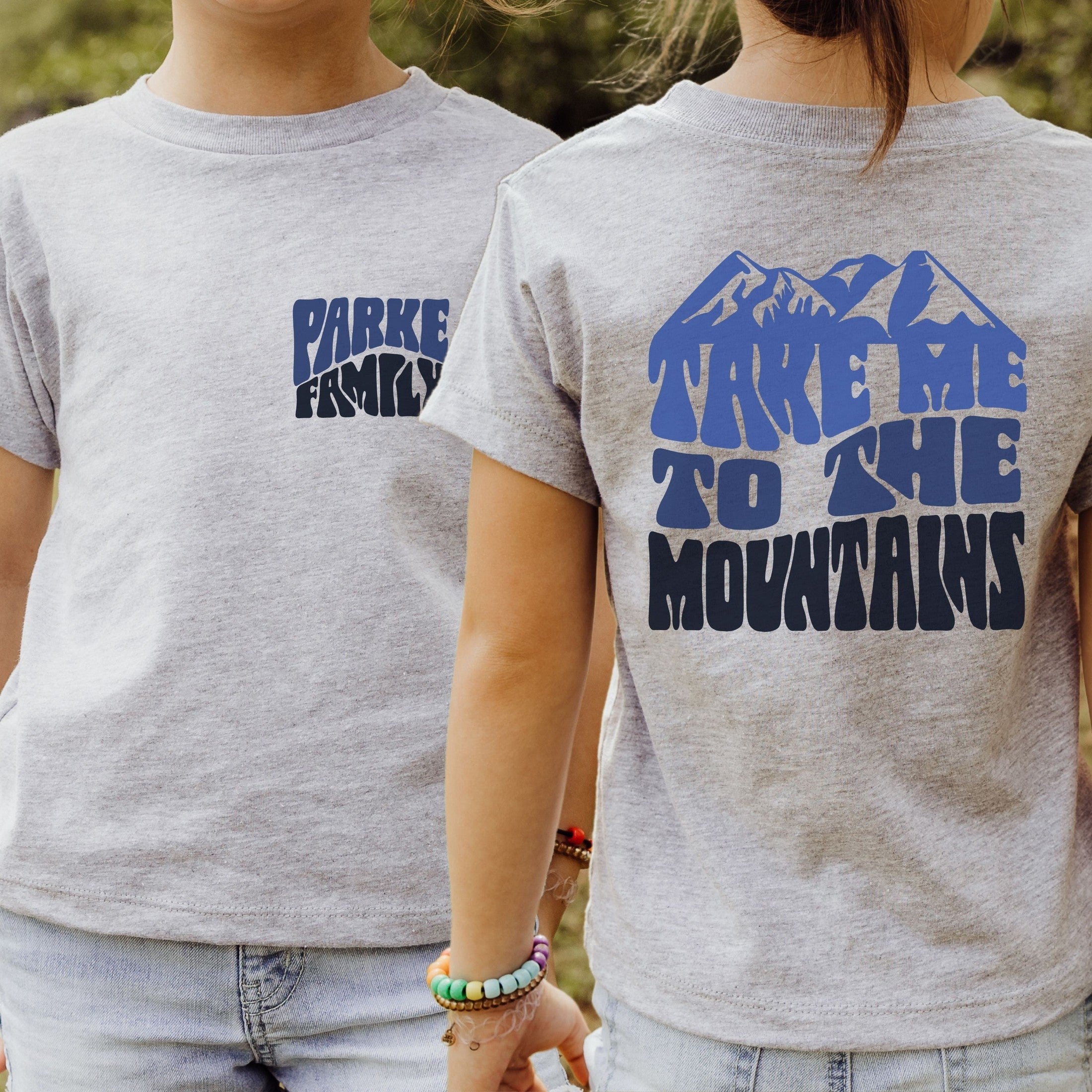 girl wearing custom matching family adventure vacation shirt with blue retro style Take Me To The Mountains design. Perfect for group ski weekends. Shown on gray tshirt