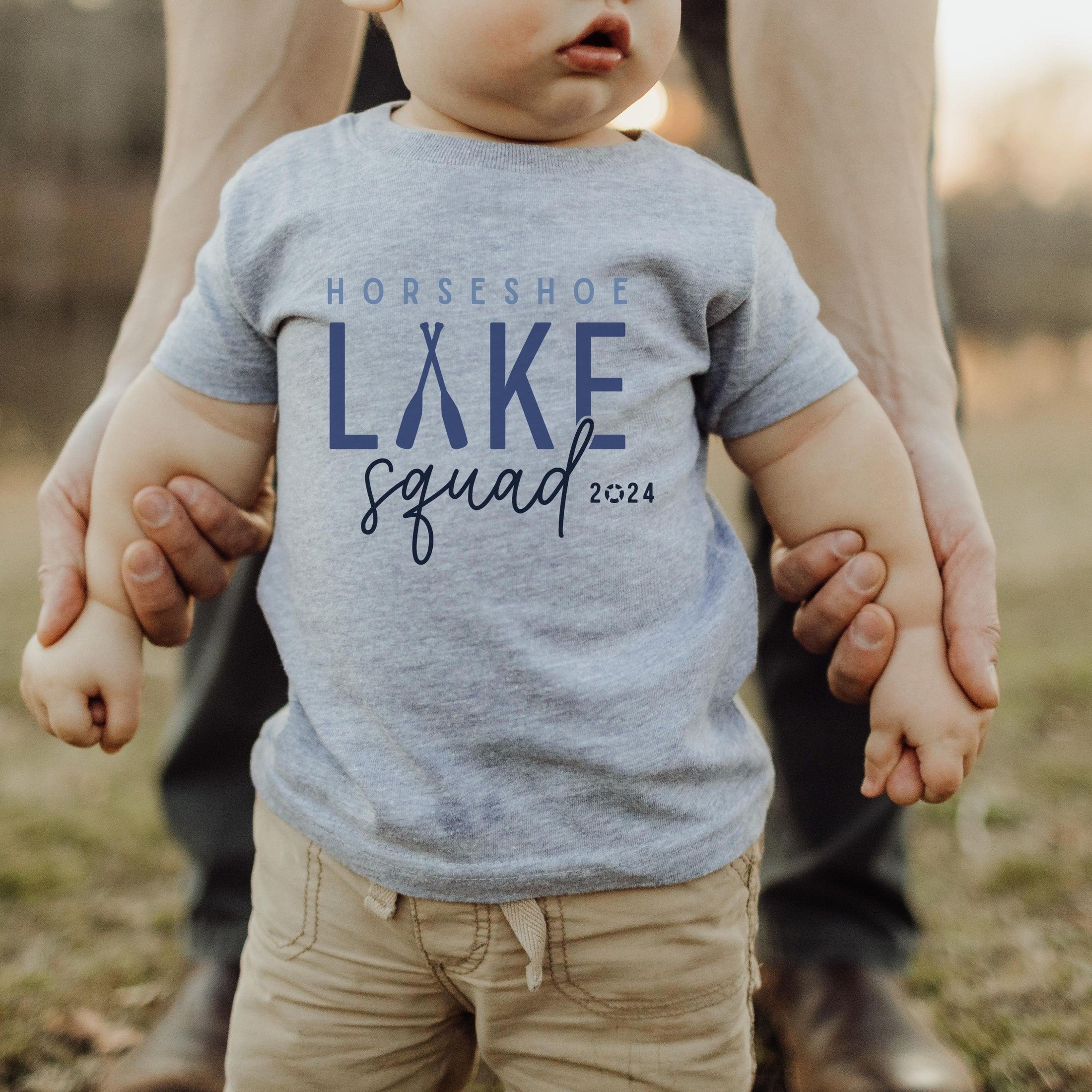 infant wearing custom matching family Lake Squad shirts personalized with name and year. Perfect for group lake vacations, shown in gray baby tshirt