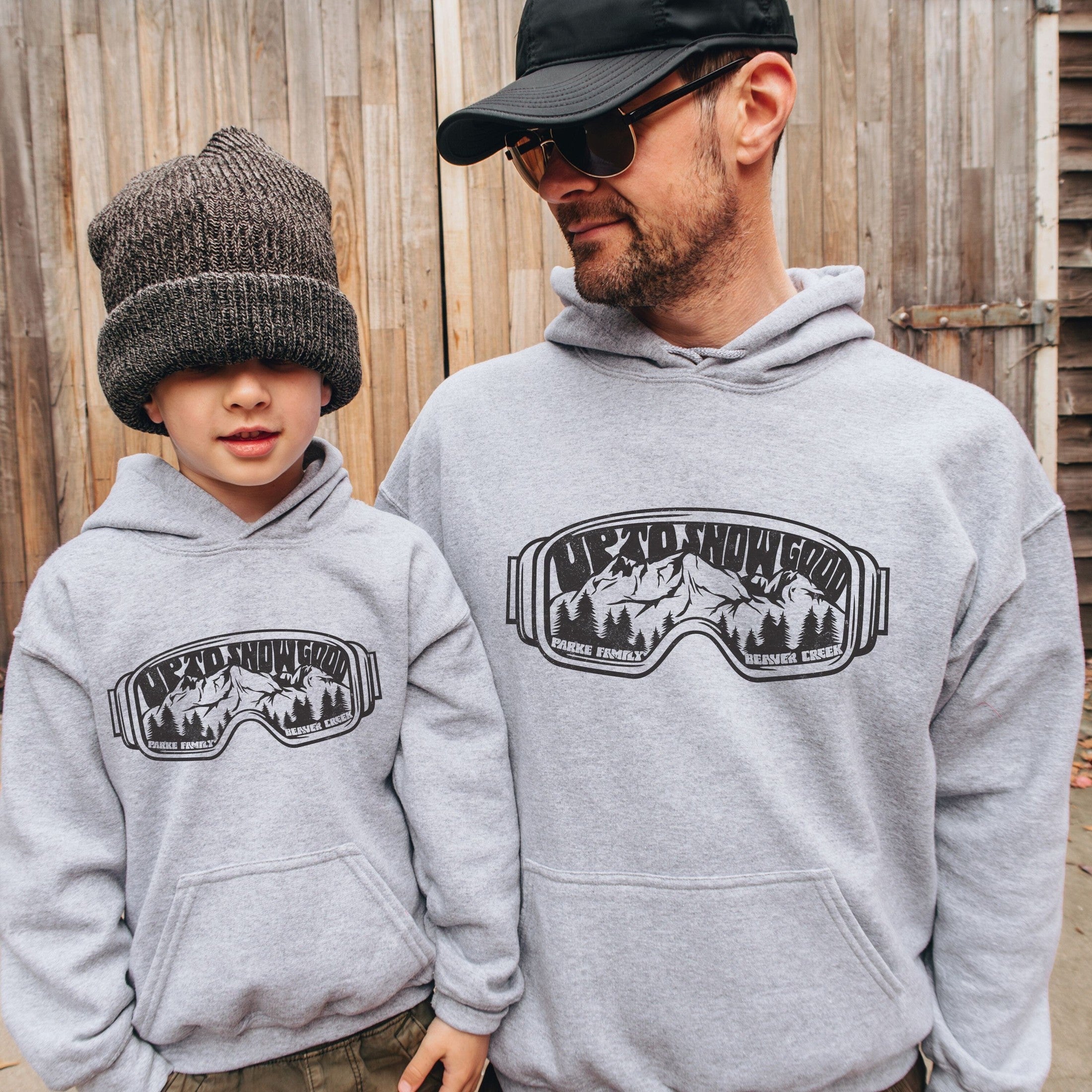 Father and son wearing Custom matching family ski trip hoodies with funny Up To Snow Good goggles design for group mountain weekend vacations shown in gray