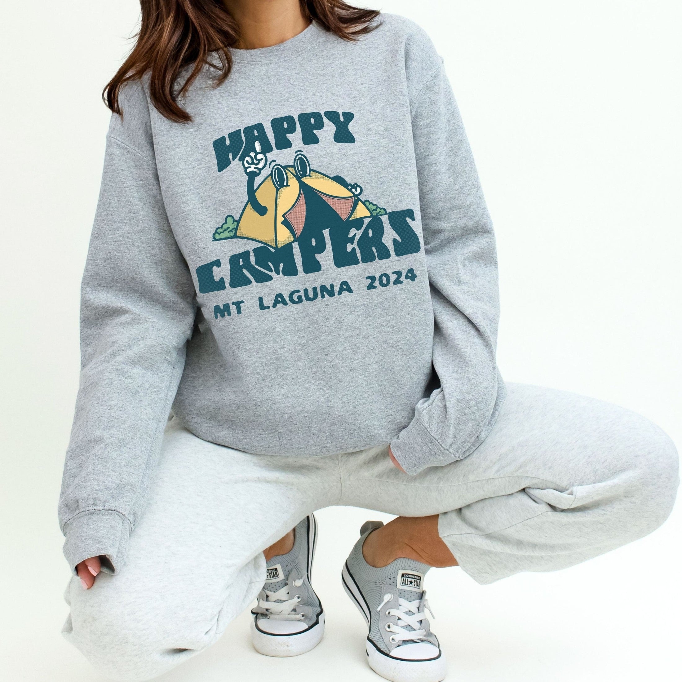 woman wearing custom matching family adventure vacation shirt with retro mascot style Happy Camper cartoon design. Perfect for group camping trips. Shown on gray crewneck sweatshirt