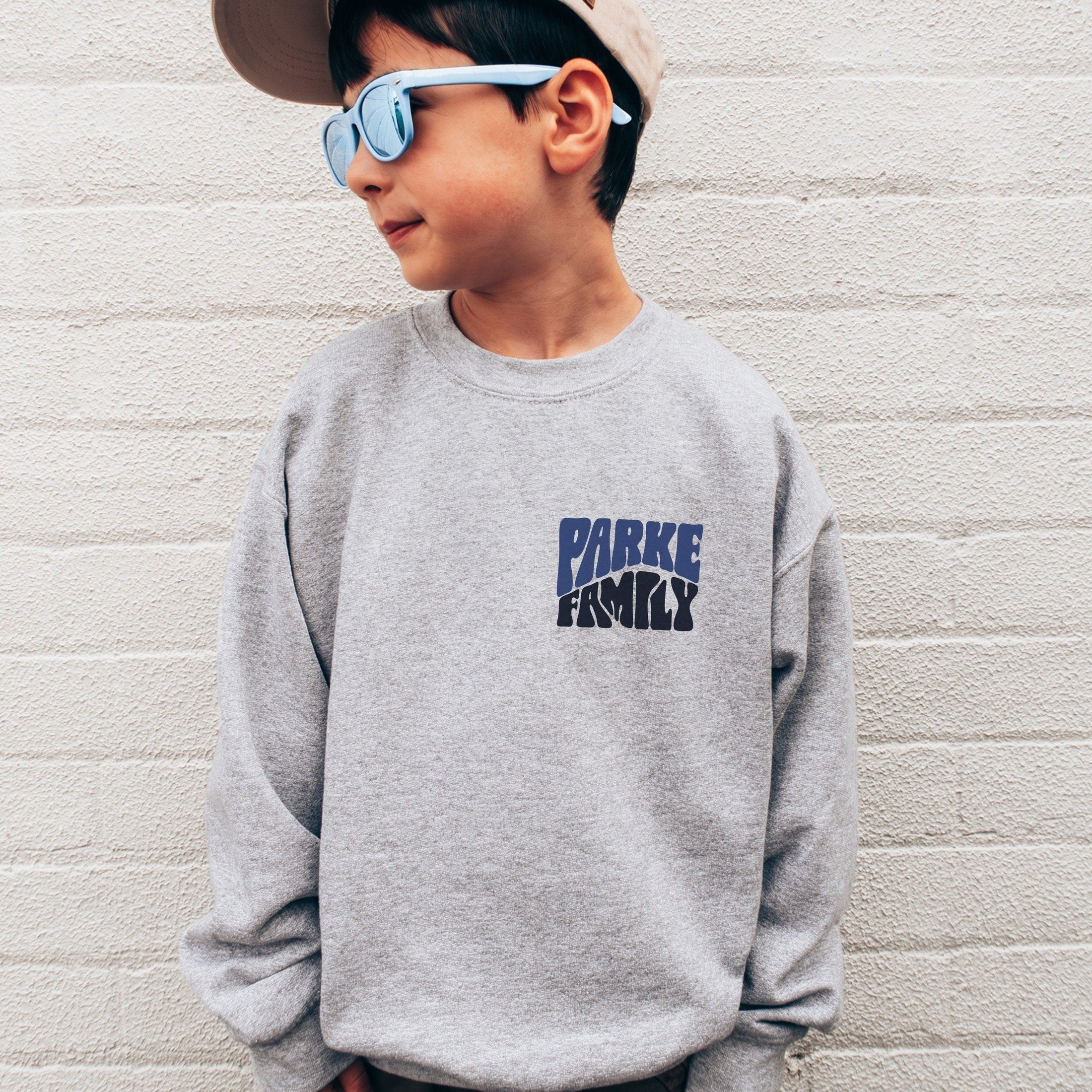 boy wearing custom matching family adventure vacation shirt with blue retro style Take Me To The Mountains design. Perfect for group ski weekends. Shown on gray crewneck sweatshirt.