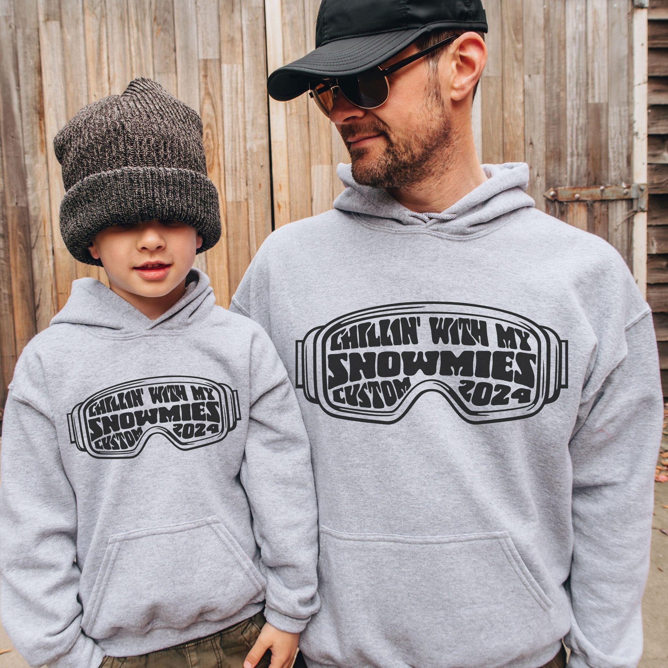 father and son wearing custom matching family winter vacation shirts with funny Chillin With My Snowmies goggles design perfect for group ski trip weekends shown on gray hoodie sweatshirts