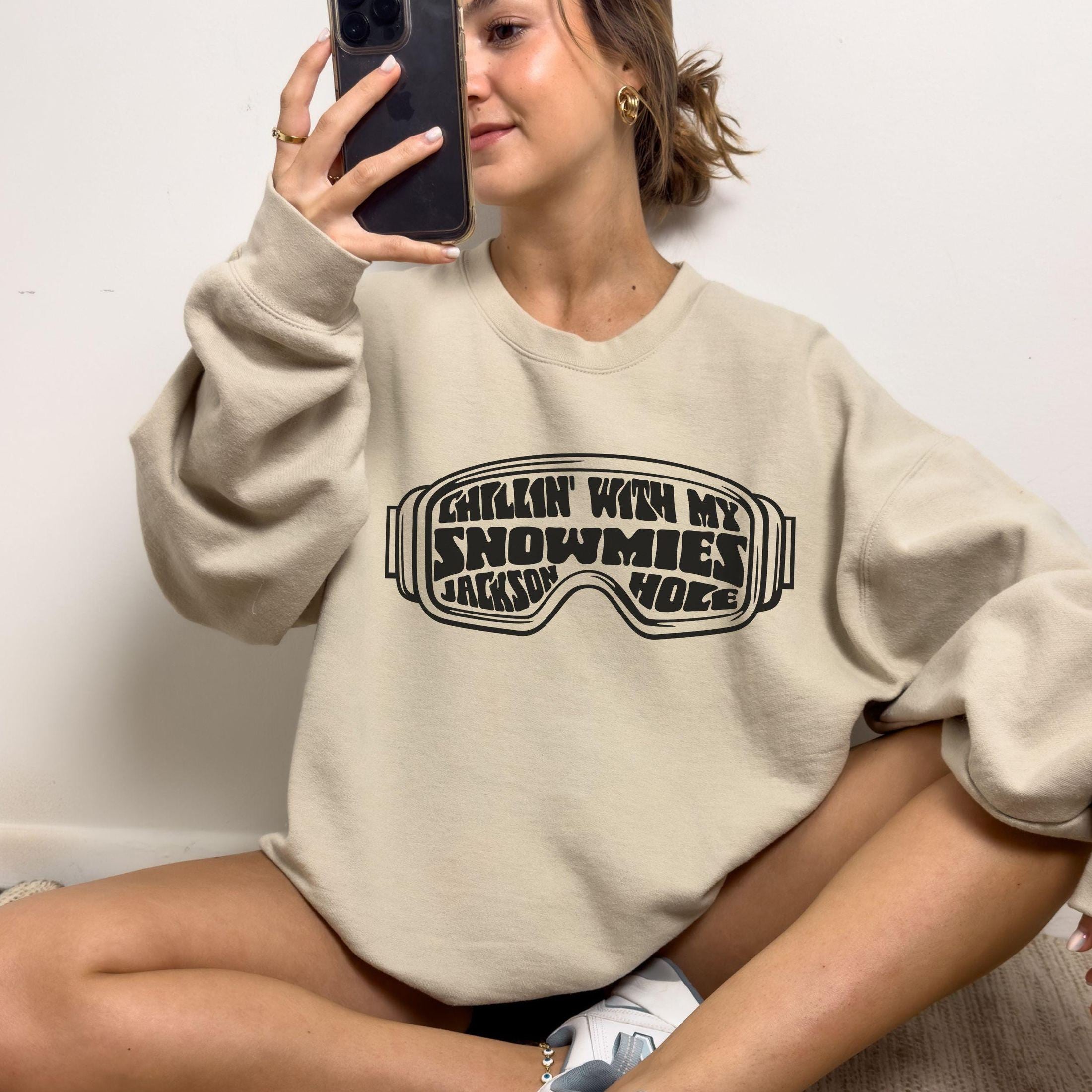 woman wearing custom matching family winter vacation shirts with funny Chillin With My Snowmies goggles design perfect for group ski trip weekends shown on sand crewneck sweatshirt