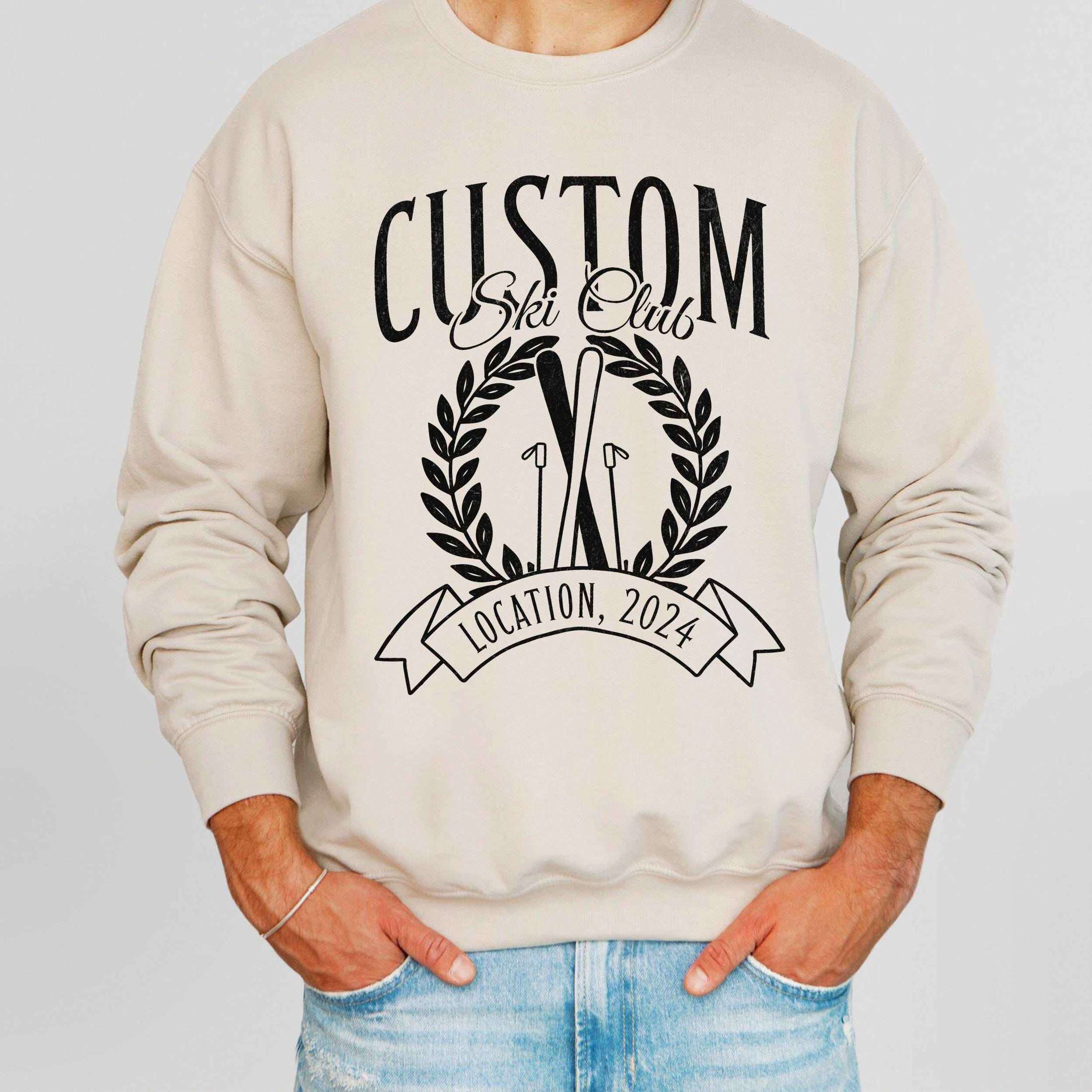 man wearing custom matching family vacation preppy ski club logo shirt for group ski weekend trips. shown in sand crewneck sweatshirt