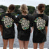 Women wearing custom matching 60s or 70s retro floral girls trip shirts for group vacation shown in Comfort Colorsblack