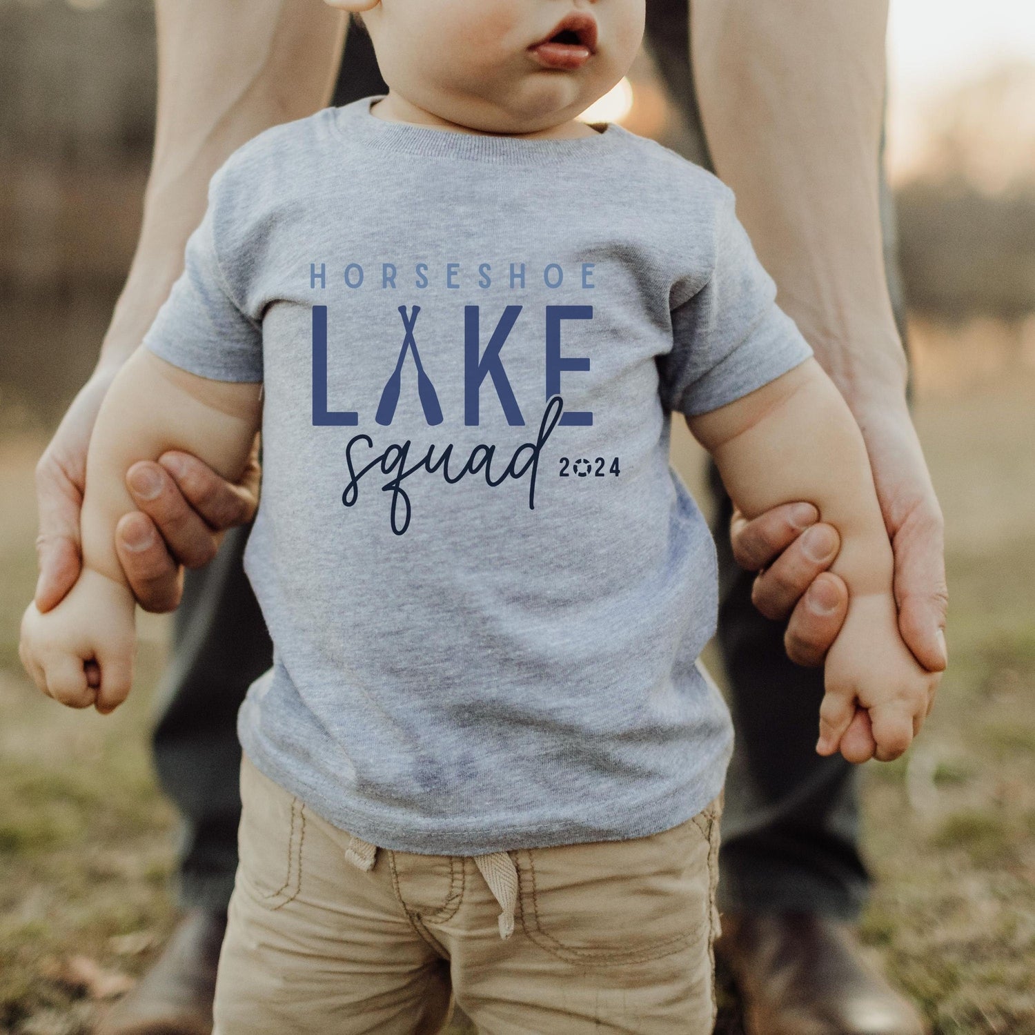 infant wearing custom matching family Lake Squad shirts personalized with name and year. Perfect for group lake vacations, shown in gray baby tshirt