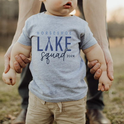 infant wearing custom matching family Lake Squad shirts personalized with name and year. Perfect for group lake vacations, shown in gray baby tshirt