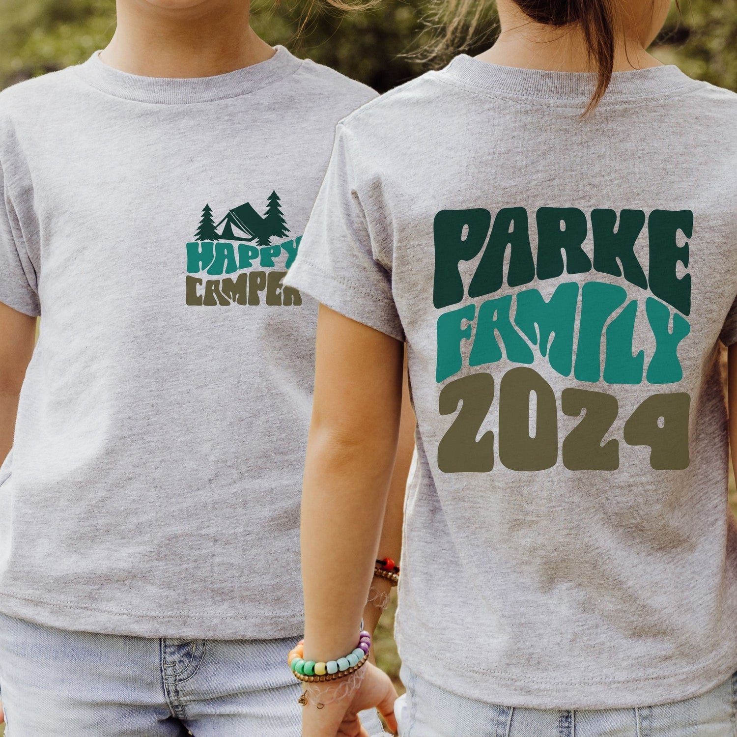 Girl wearing custom matching family adventure vacation shirt with green retro style Happy Camper design. Perfect for group camping trips. Shown on gray tshirt.